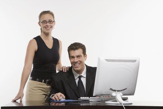 Caucasian mid-adult woman touching shoulder of man sitting at computer and looking at viewer.