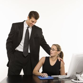 Caucasian mid-adult man touching shoulder of woman sitting at computer who feels uncomfortable.