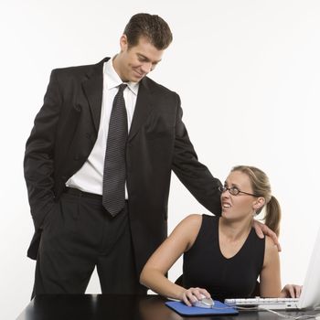 Caucasian mid-adult man sexually harassing woman sitting at computer.