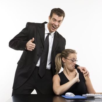 Caucasian mid-adult man sexually harassing woman sitting at computer and giving thumbs up.