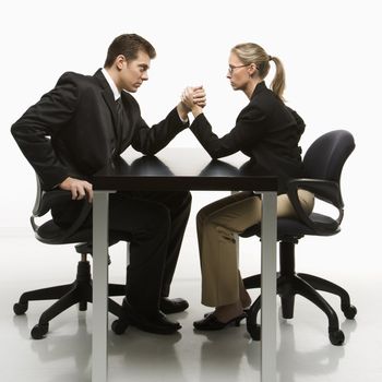 Side view of Caucasian mid-adult businessman and businesswoman arm wrestling on table.