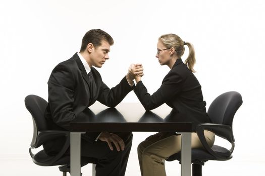 Side view of Caucasian mid-adult businessman and businesswoman arm wrestling on table.