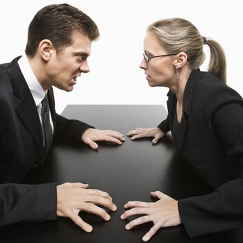 Caucasian mid-adult businessman and woman staring at each other with hostile expression.