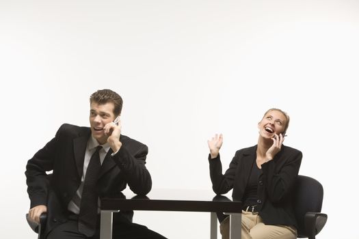 Caucasian mid-adult businessman and woman sitting and talking on cell phones.