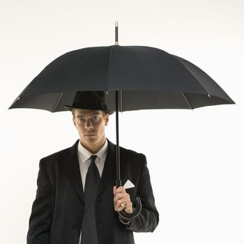 Caucasian mid-adult businessman wearing fedora holding umbrella and looking at viewer.