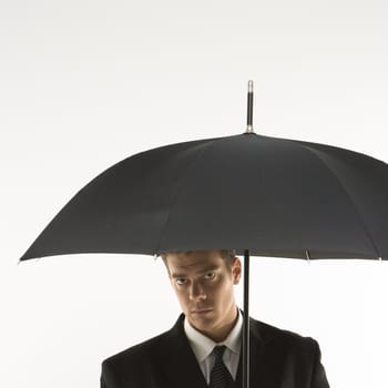 Caucasian mid-adult businessman looking out at viewer from under umbrella.