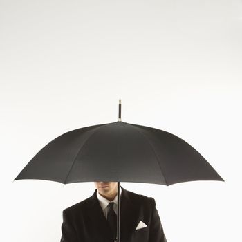 Caucasian mid-adult businessman holding umbrella with face covered.