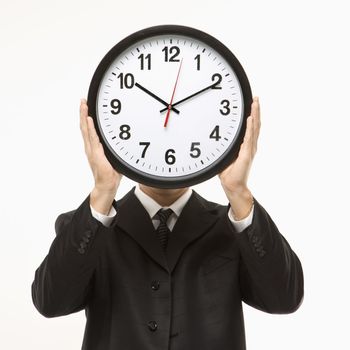 Caucasian man wearing suit holding clock in front of face.