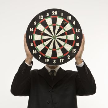 Caucasian man wearing suit and holding dartboard in front of face.