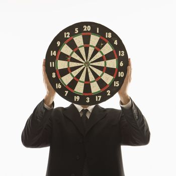 Caucasian man wearing suit and holding dartboard in front of face.