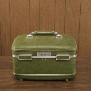 Still life shot of a vintage green luggage piece sitting on a wooden desk.