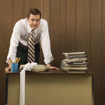 Mid-adult Caucasian male with pencil in his mouth and hands on a desk.