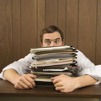 Mid-adult Caucasian male peeking over big stack of paperwork.