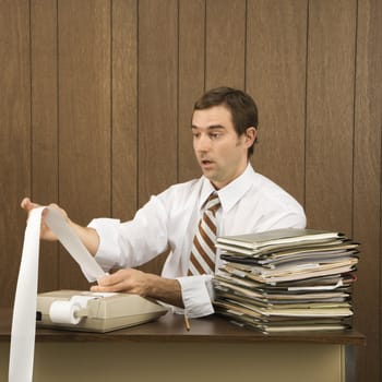 Mid-adult Caucasian male holding printout from calculator in office setting.