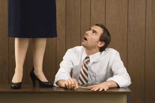 Mid-adult Caucasian male sitting at desk looking up to Caucasian female standing on desk.