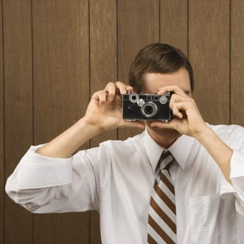 Mid-adult Caucasian male holding vintage camera up to his face.