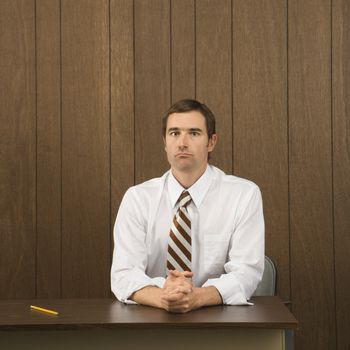 Mid-adult Caucasian male sitting at desk with pencil beside him.