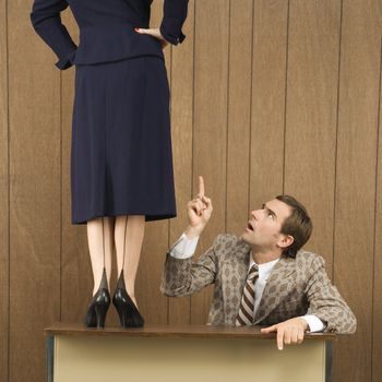 Mid-adult Caucasian male pointing up to Caucasian female standing on desk.