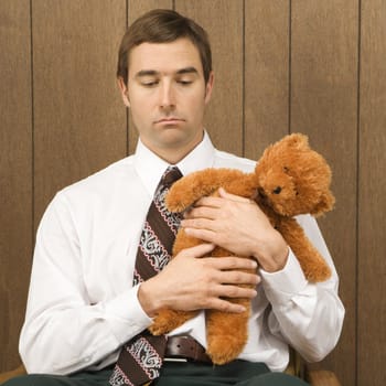 Mid-adult Caucasian male holding a stuffed animal looking sad.