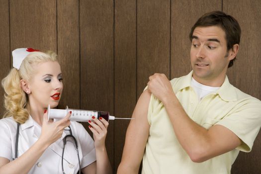 Caucasian mid-adult female nurse giving shot to man with oversized syringe.