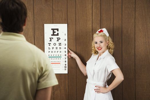 Caucasian mid-adult female nurse pointing out eye chart to mid-adult male patient.