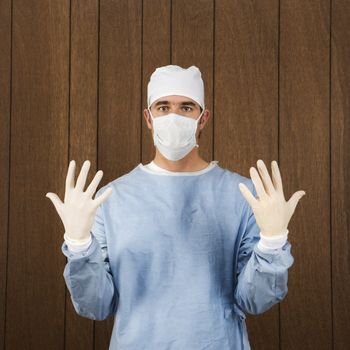 Caucasian mid-adult male surgeon wearing face mask and holding up gloved hands.