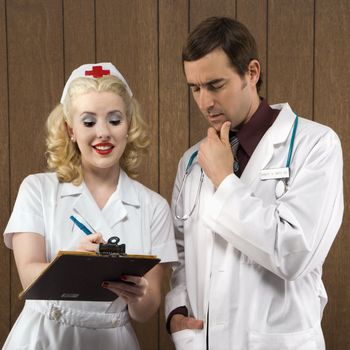 Mid-adult Caucasian female nurse and male doctor standing looking at clipboard.