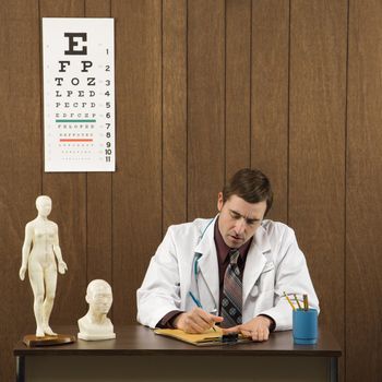 Mid-adult Caucasian male doctor sitting at desk writing.