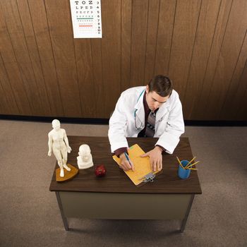 High angle of mid-adult Caucasian male doctor at desk writing.