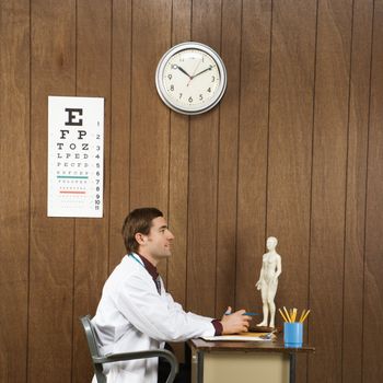 Side view of mid-adult Caucasian male doctor sitting at desk.