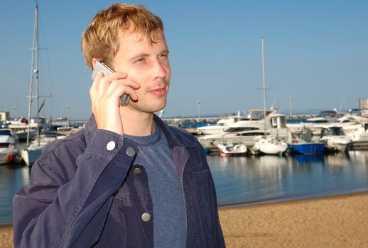 Young stylish man talk on mobile phone with yacht background.