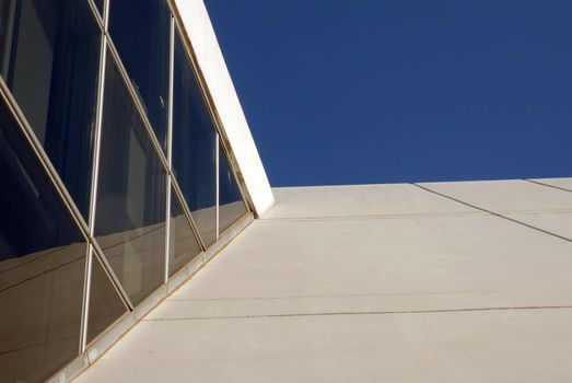 Architectural detail of a contemporary building reflecting on a blue sky background. Bottom view