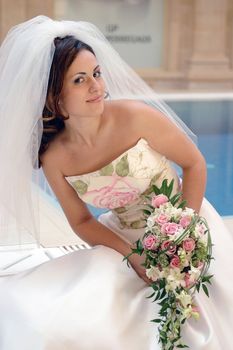 Smiling bride in white on her wedding day, holding bouquet.