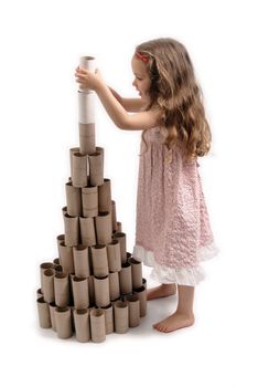 Happy little girl making a Christmas Tree with cardboard rolls of toilet paper. White background. 