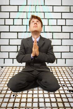 Comic businessman sitting on his knees praying