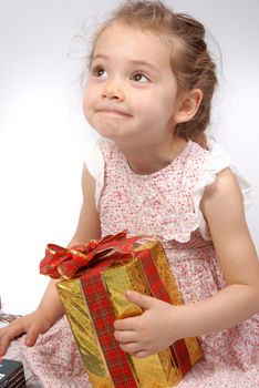 Little girl wondering about the content of her Christmas present with a funny gesture in her face. White background