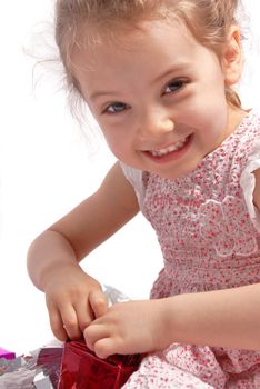 Little girl with a Christmas present smiling and looking at the camera. White background