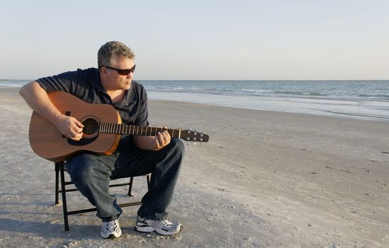 A middle aged man playing a guitar at the ocean.