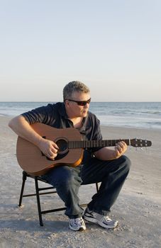 A middle-aged man playing at guitar at the ocean.