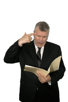 A middle-aged man pointing his finger at his head while reading from a folder.