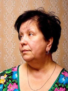 Portrait of the elderly woman in a multi-colored dress in a room