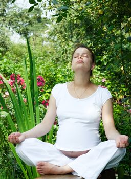 Young pregnant woman meditating at summer garden