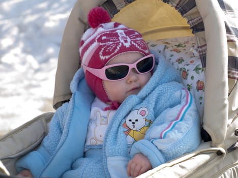 The small child in the dark glasses, sitting in a carriage.