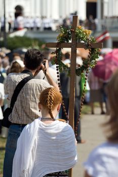 Young woman carrying cross through crowd at Day of the Assumption of Mary (15th August) Aglona, Latvia.