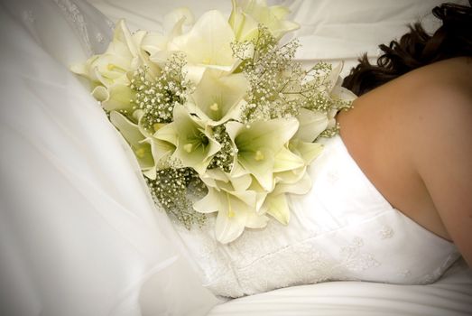 bride laying on bed with white flower bouquet on her back