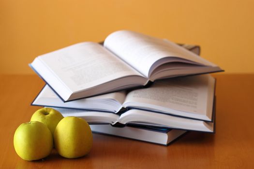 three green apples and four opened books on the desk