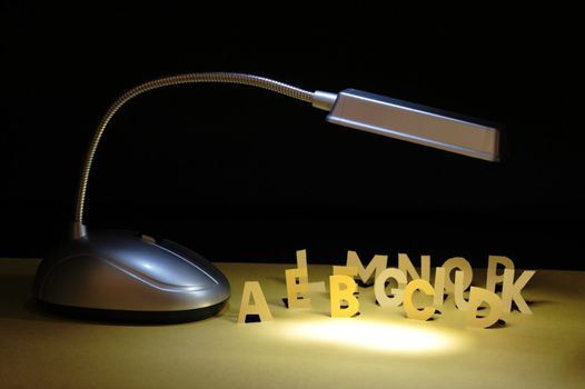 Luminous table lamp and letters cutting from yellow paper standing on dark background