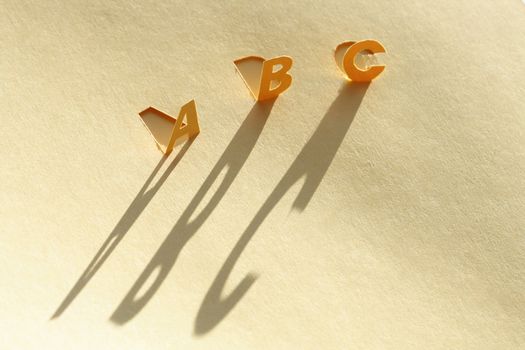 Letters A,B,C cutting from paper. Letters standing with long shadows on paper background