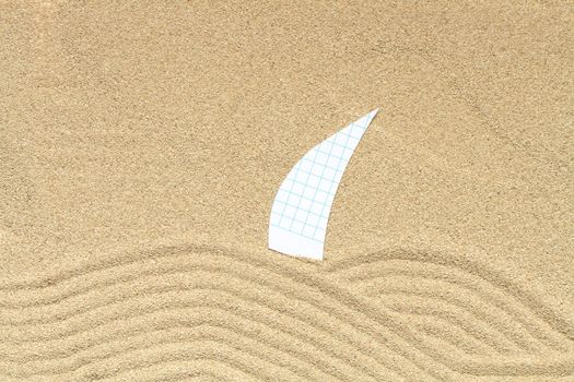 Paper sail lying on sand background with drawing waves