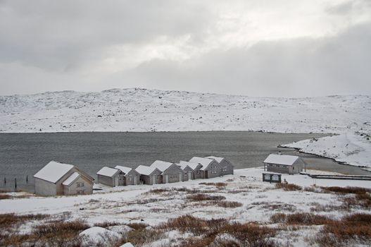 First winter snow at a mountain lake. Boathouses at the beach